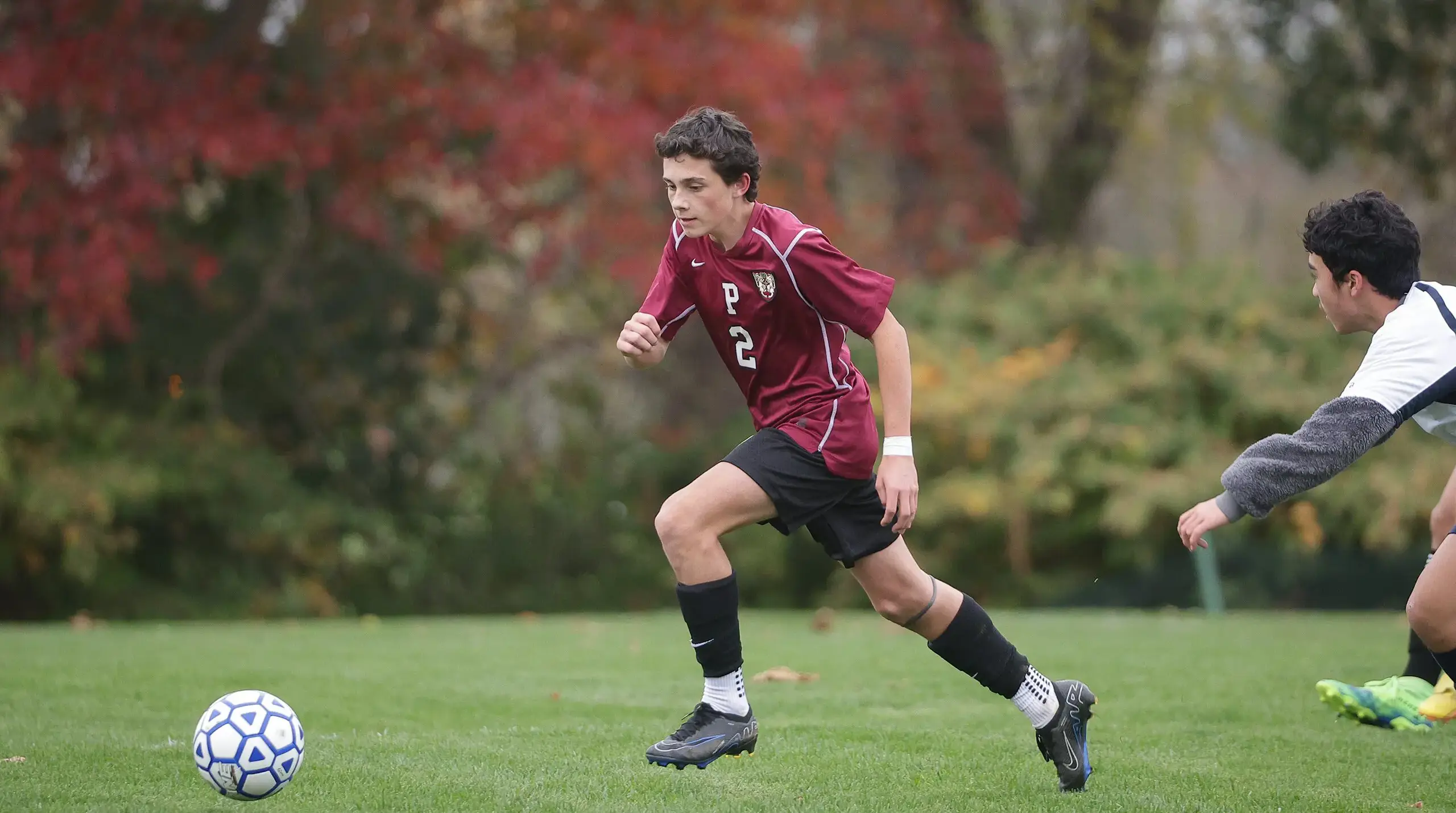 Student mid run kicking a soccer ball.