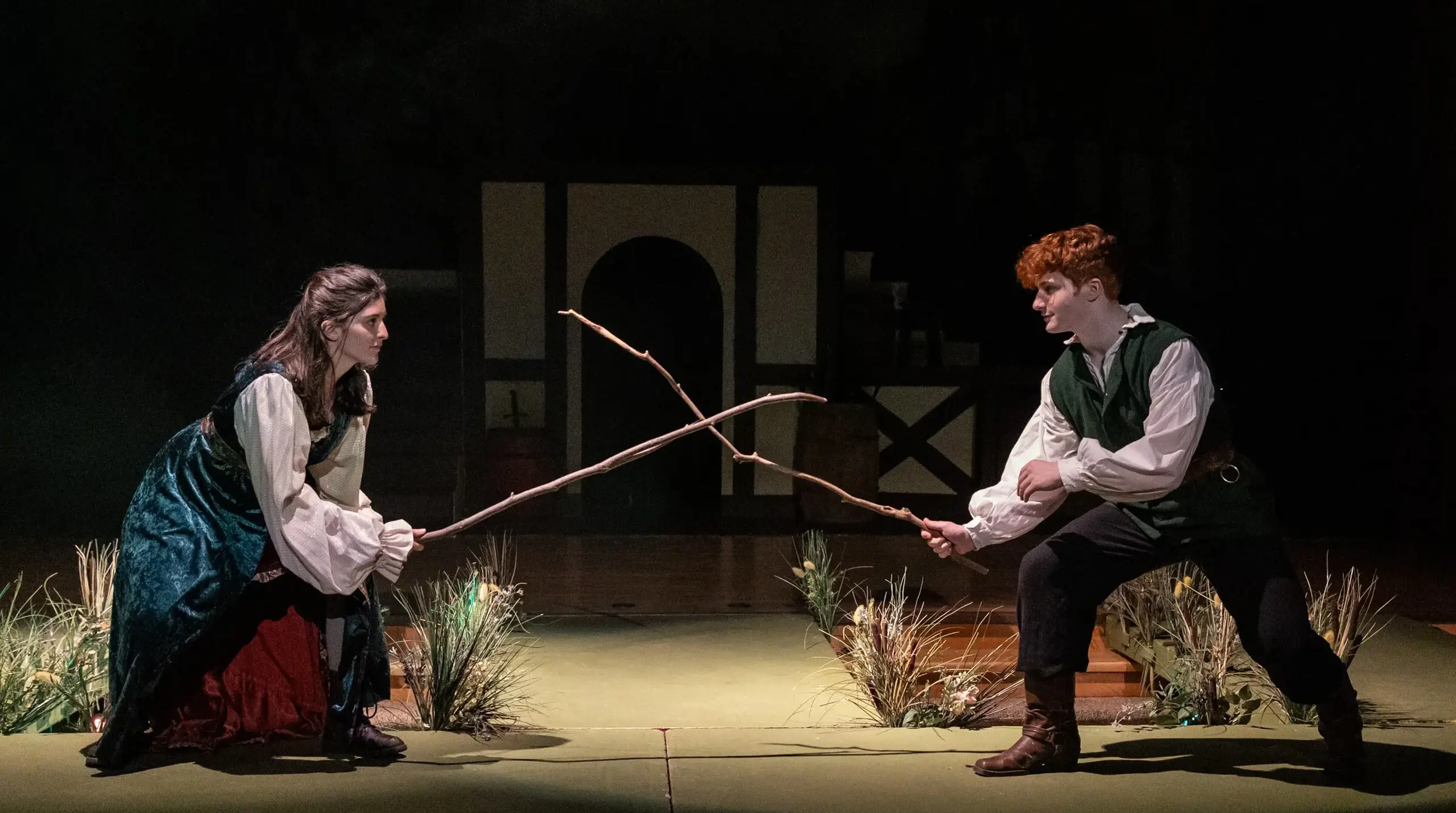 Two students using sticks to sword fight in a play.